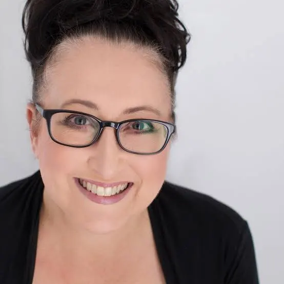 Smiling woman wearing glasses and a black top, looking at the camera with a friendly expression, updo hairstyle.