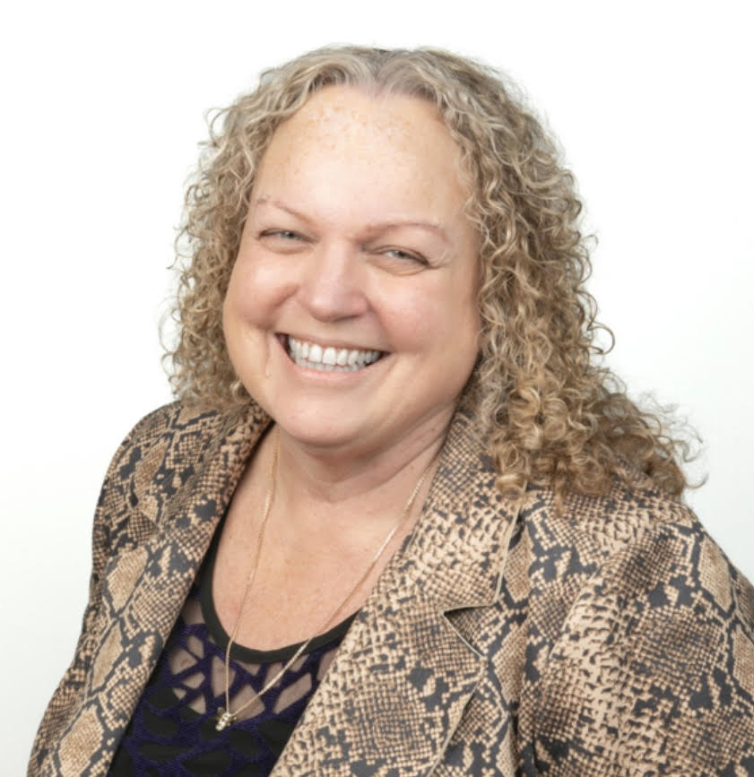 Screenshot Smiling woman with curly blonde hair wearing a snakeskin blazer and dark top.Confidence-friendly business portrait.